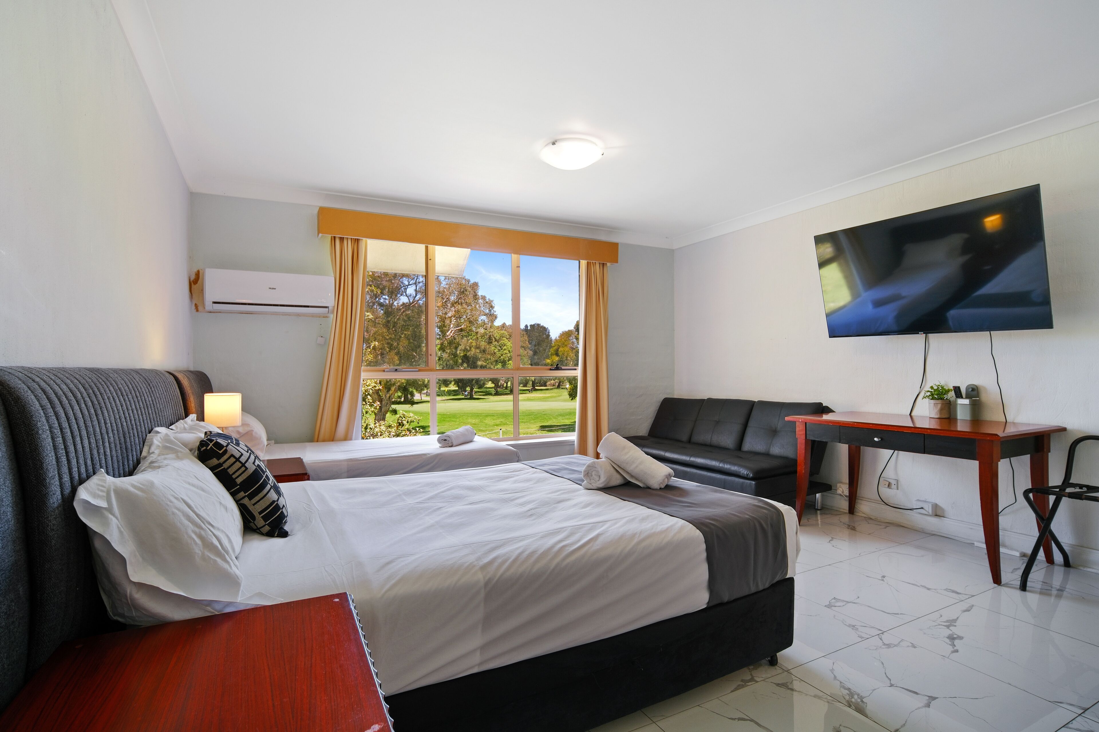 A hotel room with a bed, a desk, a TV, and a window with a view of a golf course.