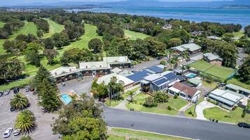 An aerial view of a residential area with a large building featuring solar panels, a swimming pool, and a golf course in the background.