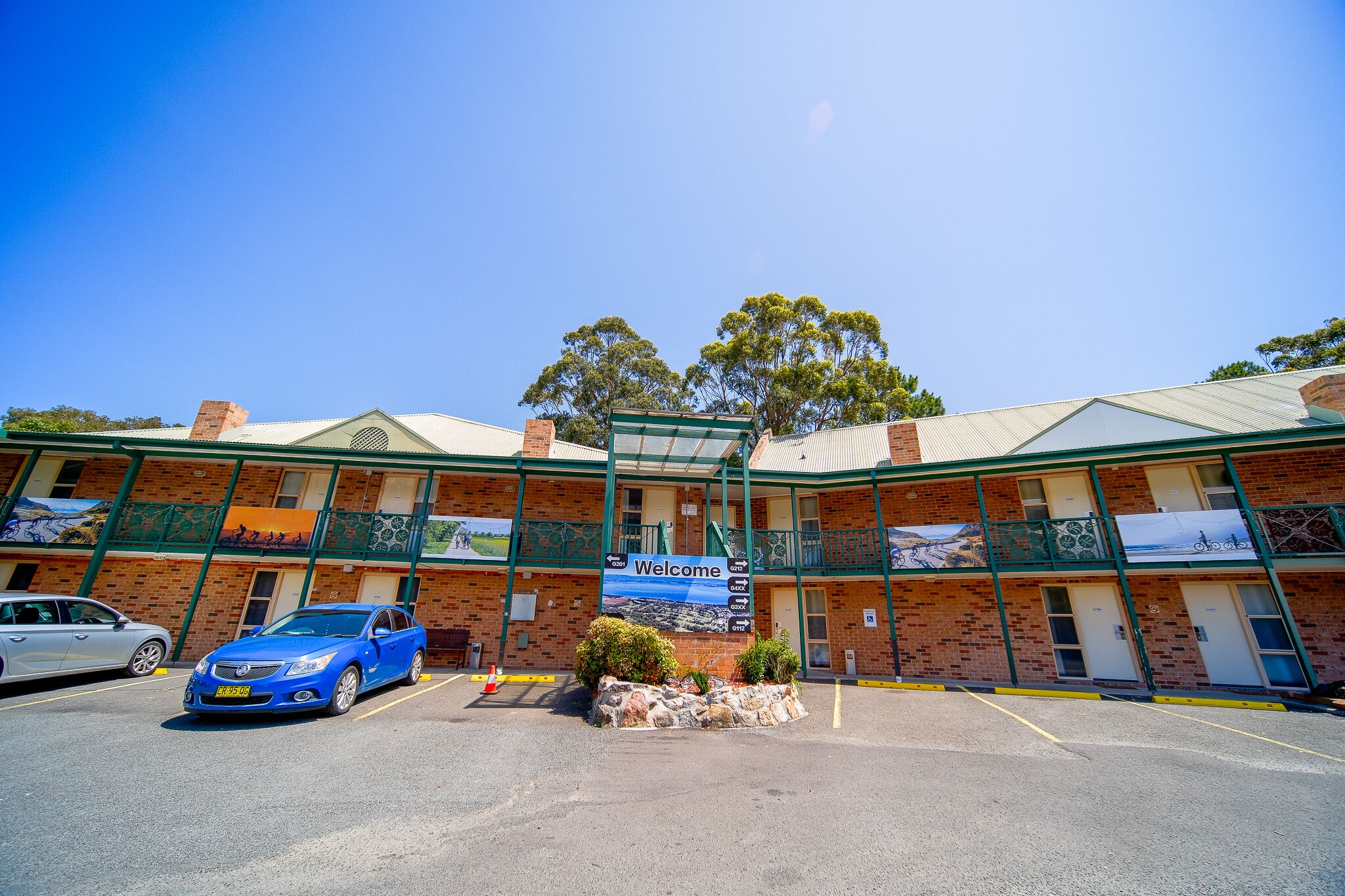 A building with a 'Welcome' sign, a parking lot, and a blue car parked in front.