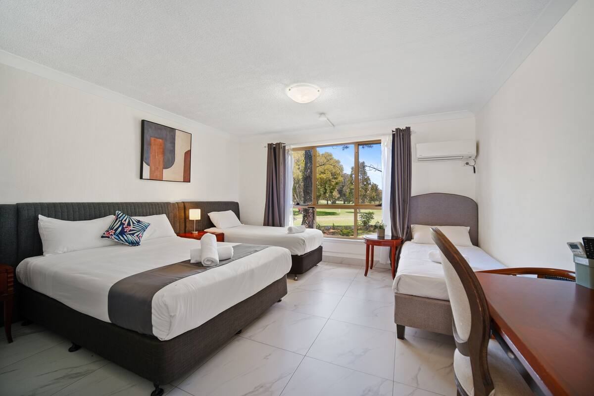 A hotel room with two beds, a desk, and a view of the outdoors.