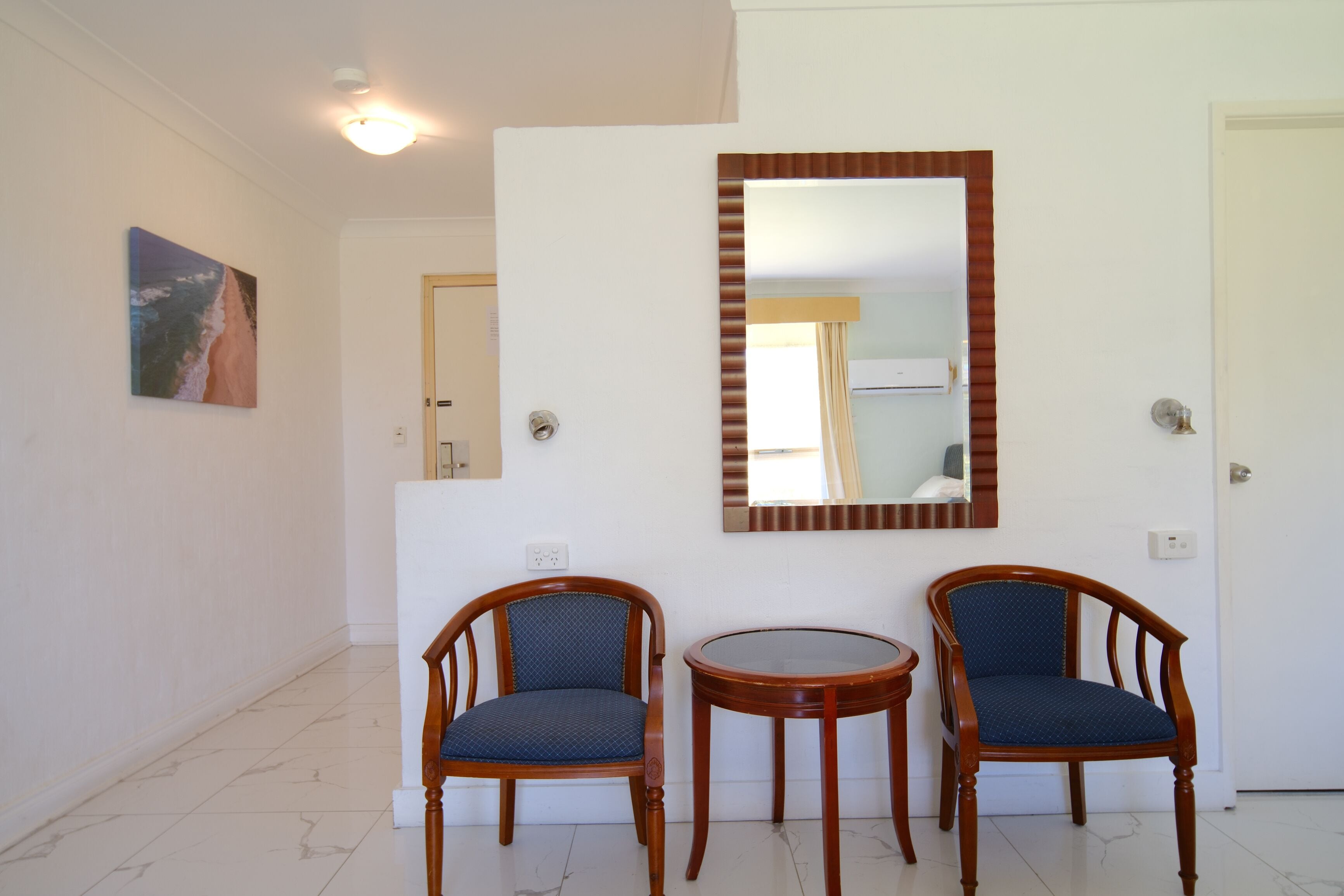 Une pièce comprenant deux chaises en bois, une petite table ronde et un grand miroir accroché au mur.