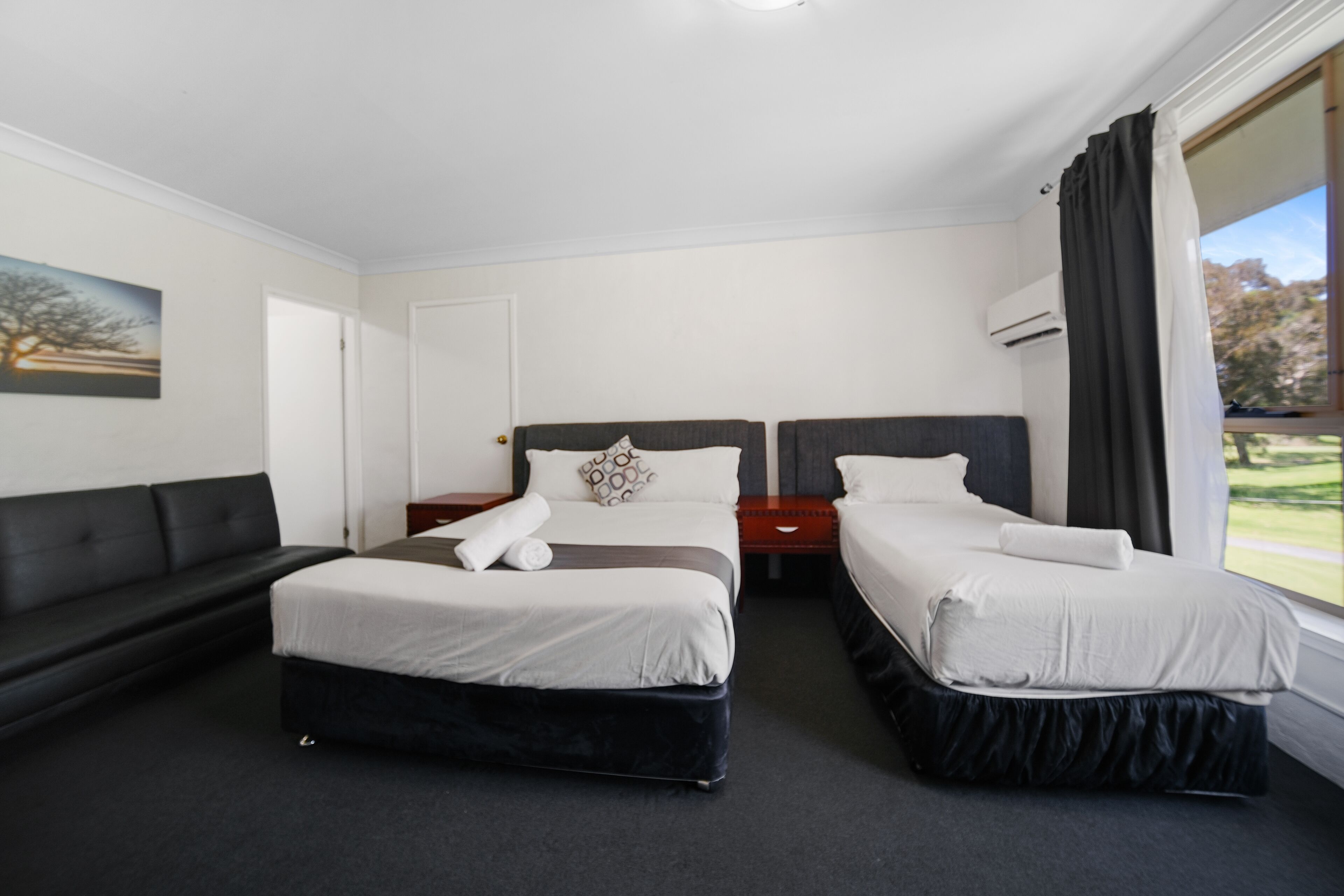 Quarto de hotel com duas camas, um sofá e uma janela grande com vista para o verde.