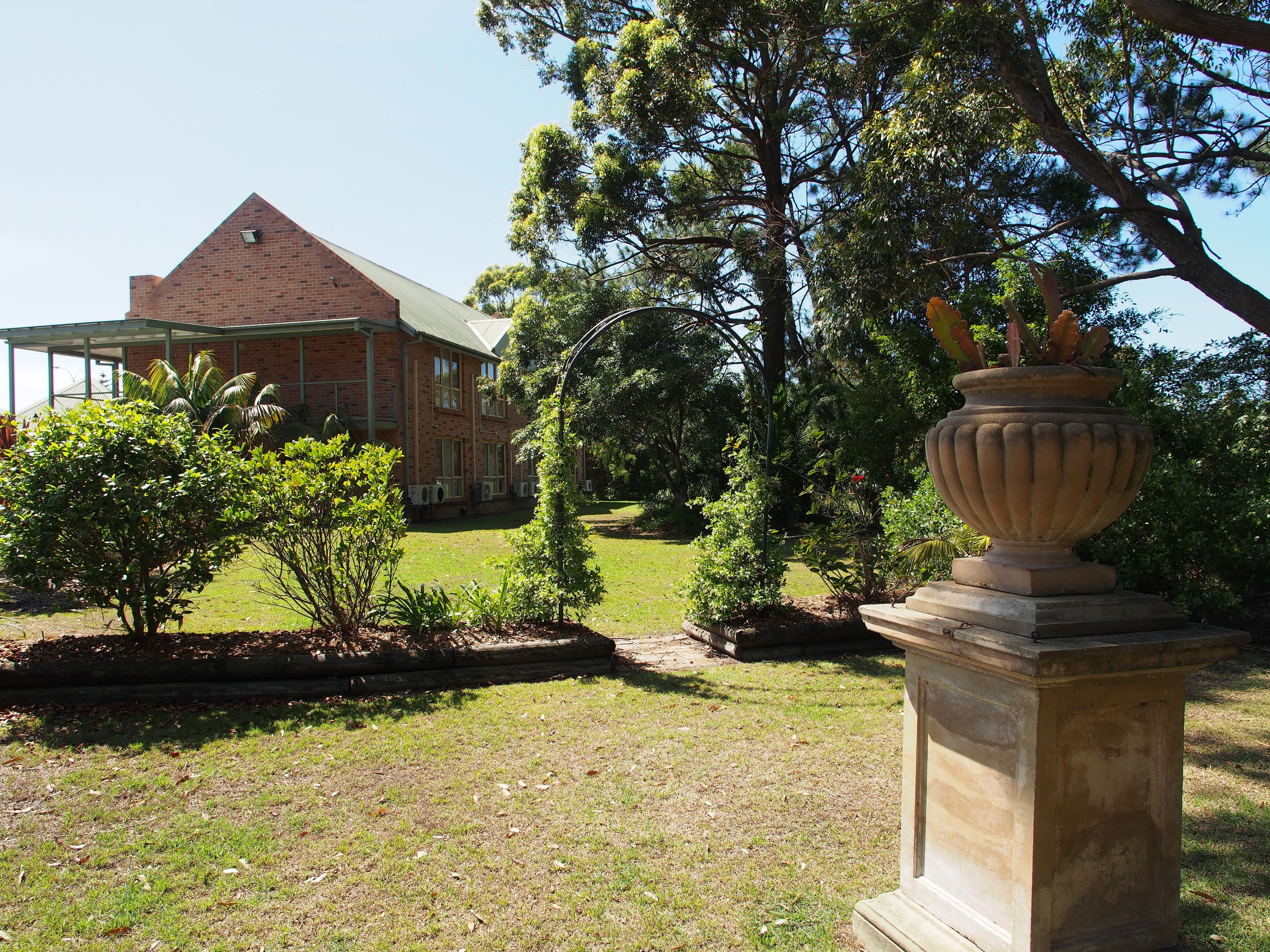 A brick building with a large lawn and a decorative urn in the foreground.
