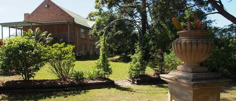 A brick building with a large lawn and a decorative urn in the foreground.