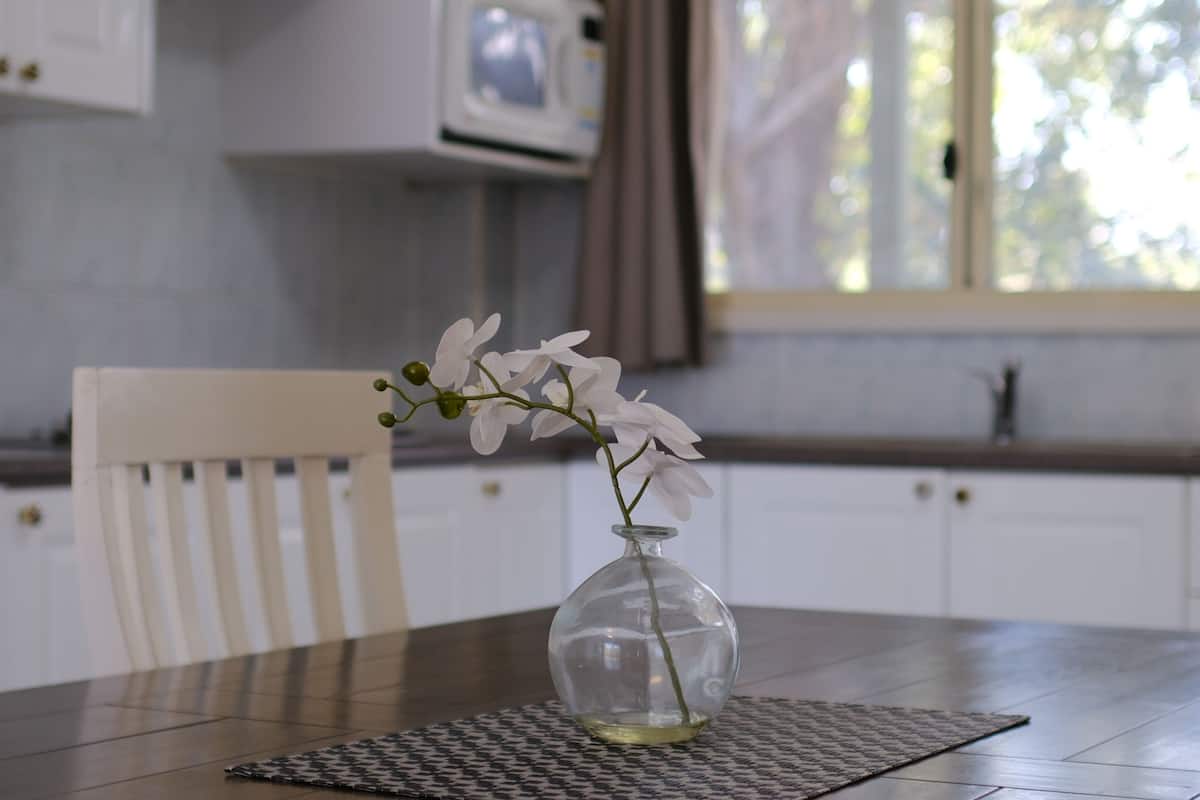 A dining table with a vase of white flowers, a patterned placemat, and a white chair.