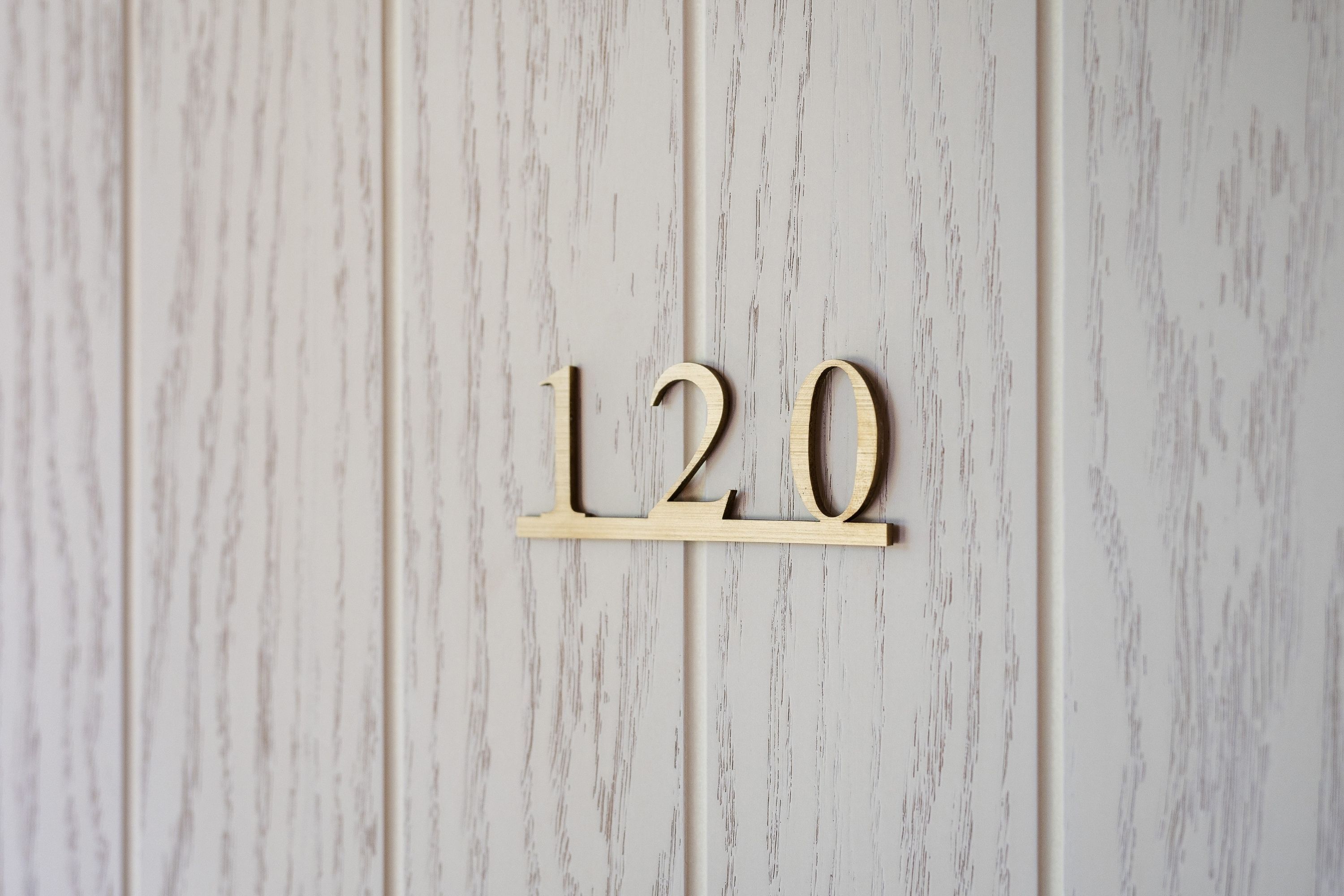 A wooden number plaque with the numbers '120' mounted on a wall with a wood grain texture.