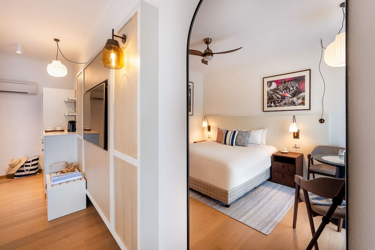 A modern hotel room with a bed, bedside table, chair, and a small desk with a chair.