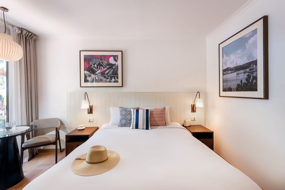 A hotel room with a large bed, two bedside tables, a chair, a desk, and two wall-mounted lamps.