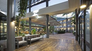 Un espacio interior amplio con suelo de madera, arreglos de asientos y vista a un edificio de varios pisos con balcones.