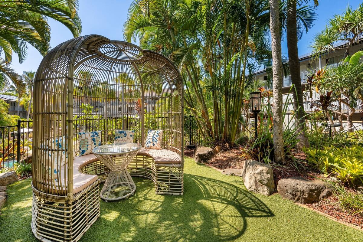 A bamboo gazebo with seating, surrounded by tropical plants and palm trees.