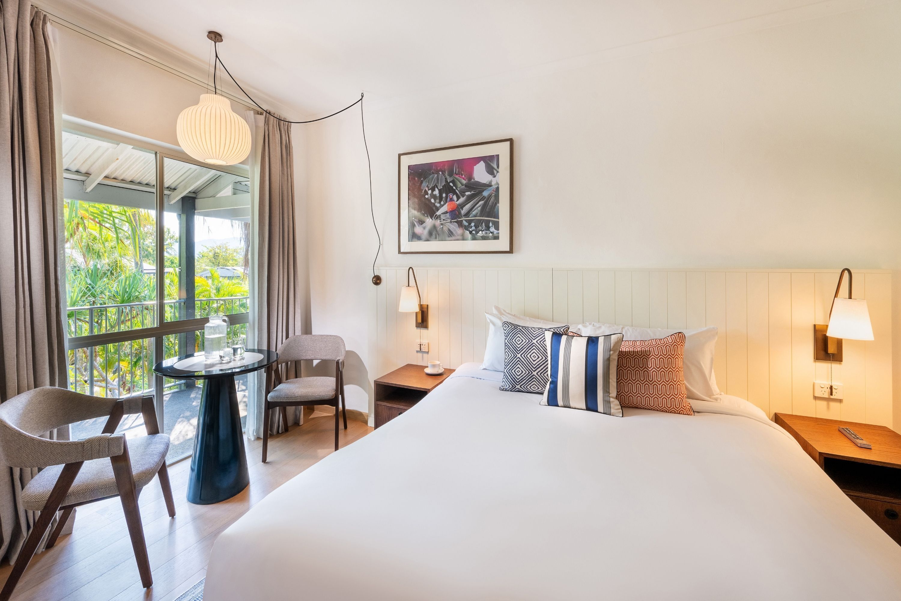 Une chambre d’hôtel avec un grand lit, un bureau avec une chaise, une table avec une chaise, une fenêtre avec des rideaux et un tableau accroché au mur.