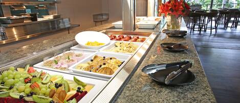 A buffet with various food options including fruits, pastries, and desserts.