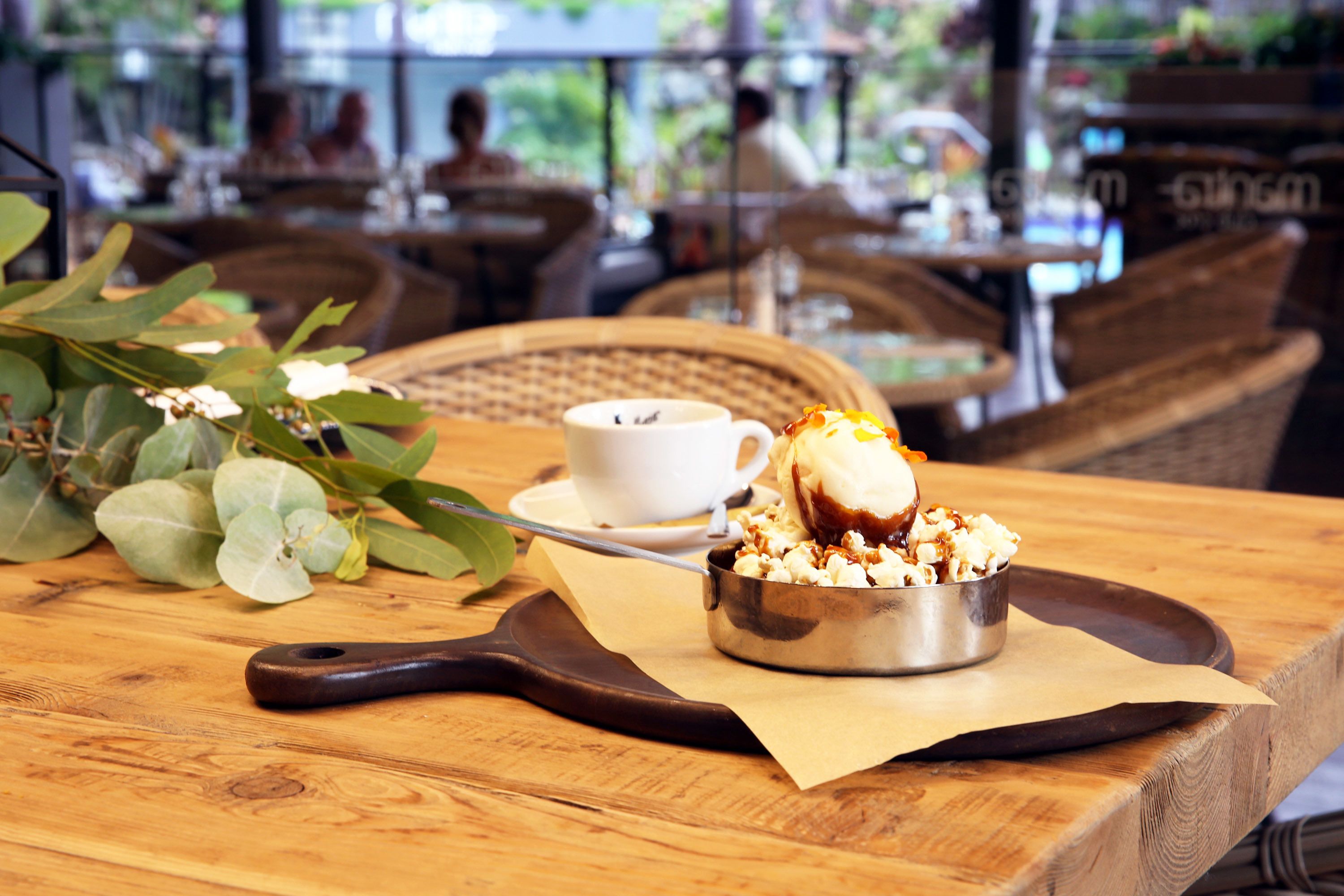A dessert with ice cream and caramel sauce on a tray, a cup of coffee, and a wooden table with a spoon.