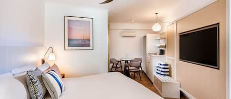 A modern hotel room with a large bed, a ceiling fan, a dining area with a table and chairs, and a TV mounted on the wall.