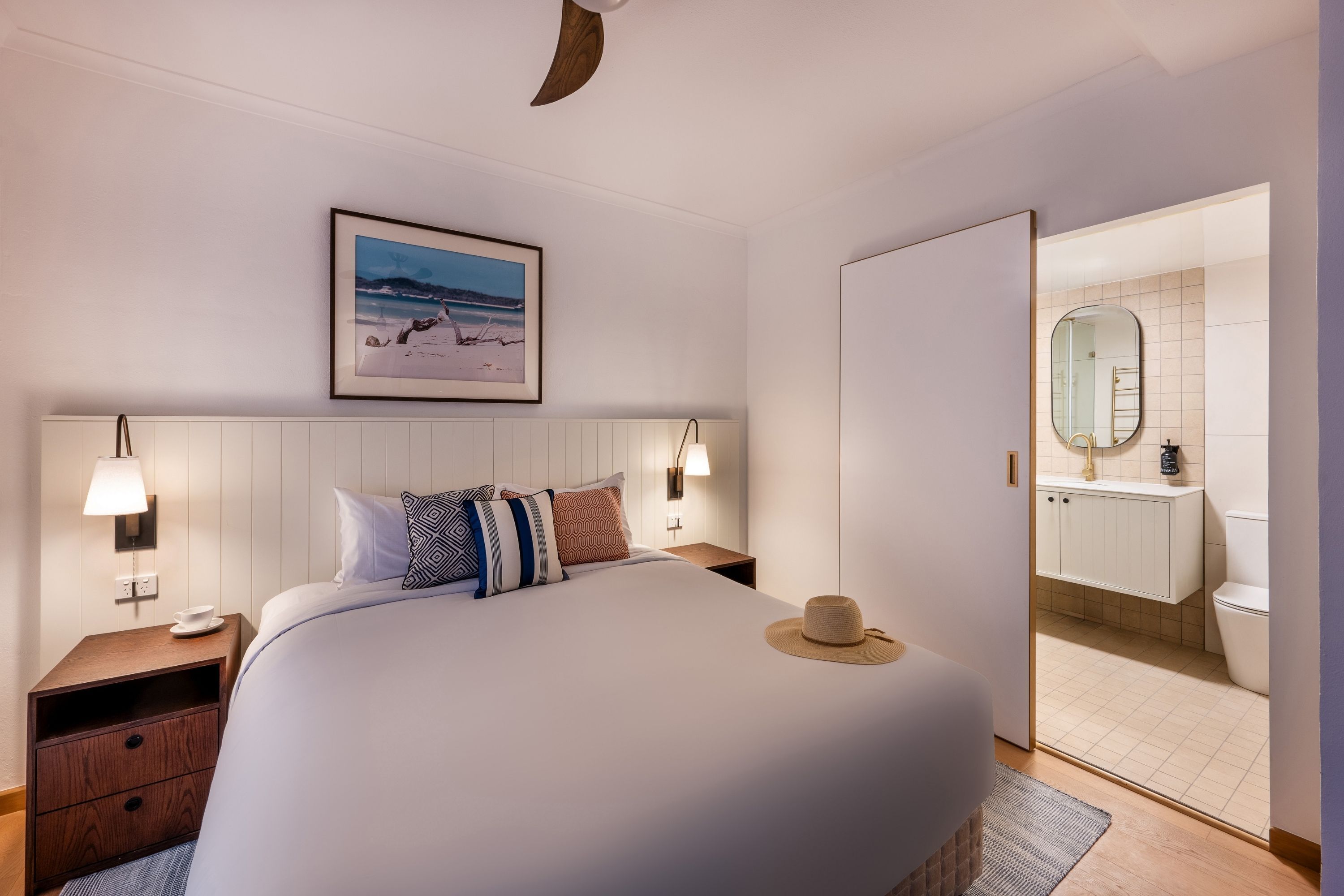 Habitación de hotel impecable con una cama grande, mesitas de noche, un cuadro en la pared y vistas al baño.