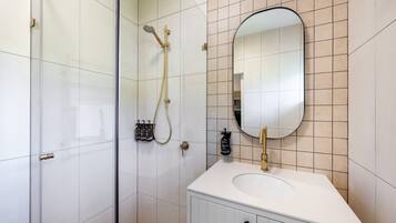 A modern bathroom with a glass shower enclosure, a white sink with a gold faucet, and a mirror with a gold frame.
