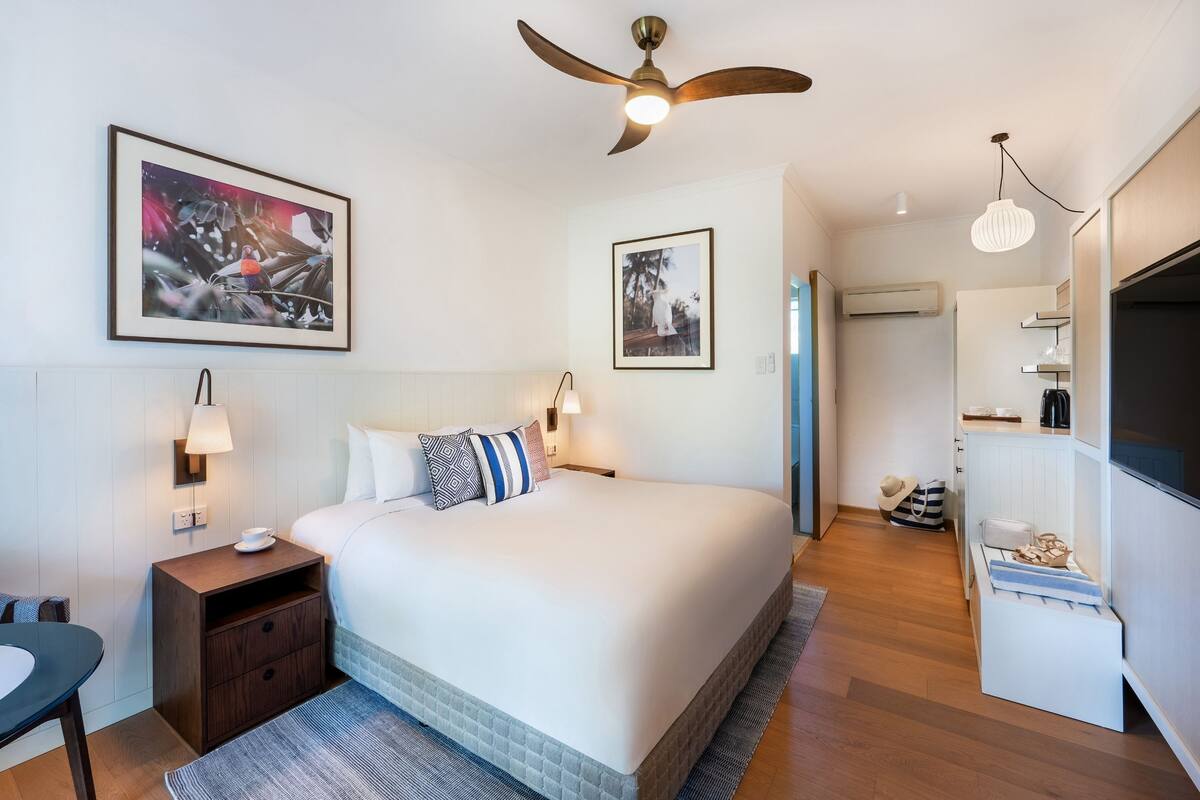 A neatly arranged bedroom with a bed, bedside tables, a ceiling fan, and artwork on the walls.