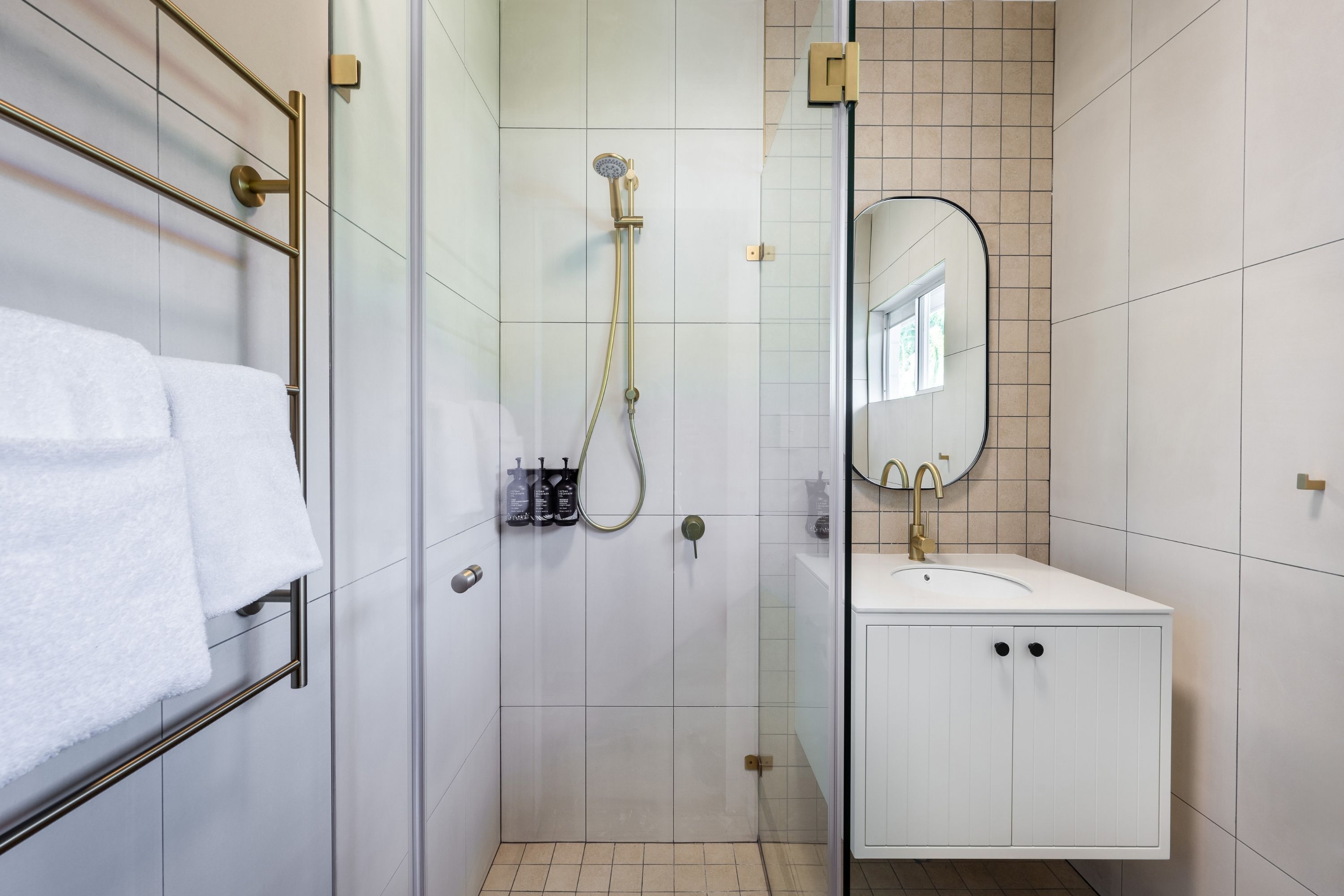 A modern bathroom with a glass shower enclosure, a white sink, and a towel rack.