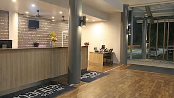 A modern reception area with a wooden reception desk, a flat-screen TV, and a large window overlooking a parking area.
