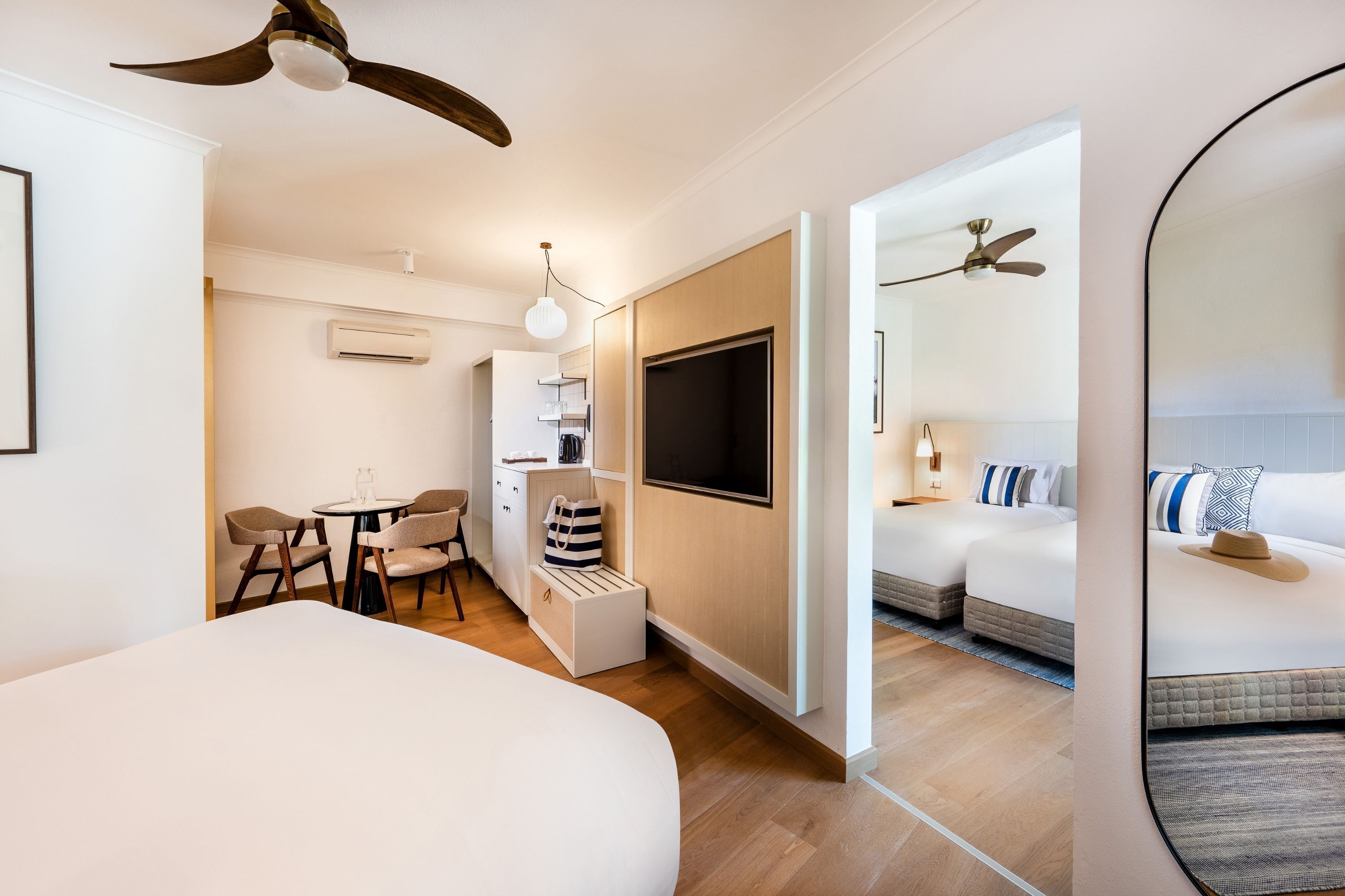 A modern hotel room with a large bed, a desk with chairs, a TV, and a ceiling fan.