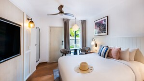 Habitación de hotel con una cama grande, ventilador de techo, televisor, mesa de comedor con sillas y vistas al exterior.