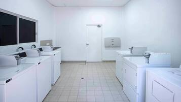 A laundry room with multiple washing machines and dryers, a white door, and a hand dryer on the wall.