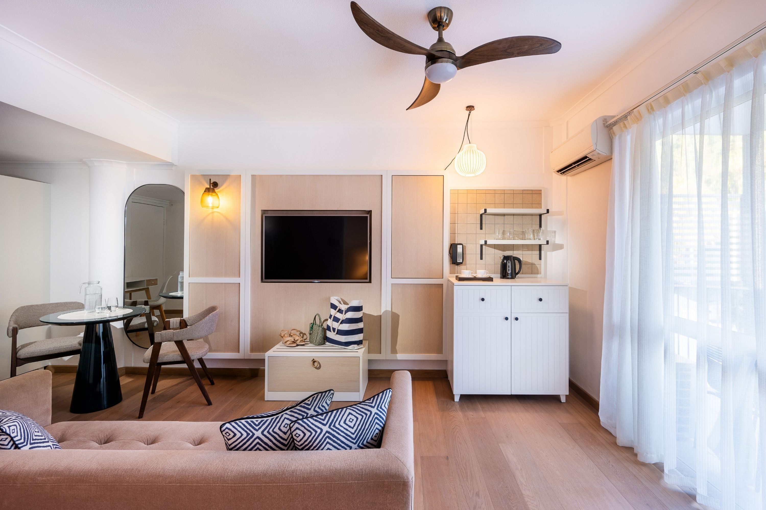 A modern living room with a sofa, a dining table, a TV, and a kitchen area with cabinets and a ceiling fan.