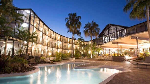 Un hotel moderno con piscina, palmeras y zonas de estar al aire libre.