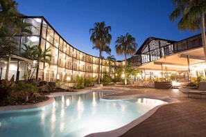 A modern hotel with a pool, palm trees, and outdoor seating areas. - Mantra Club Croc (Cannonvale)