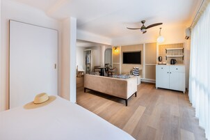 Una habitación de hotel moderna con sofá, una mesa de comedor, televisor y kitchenette.