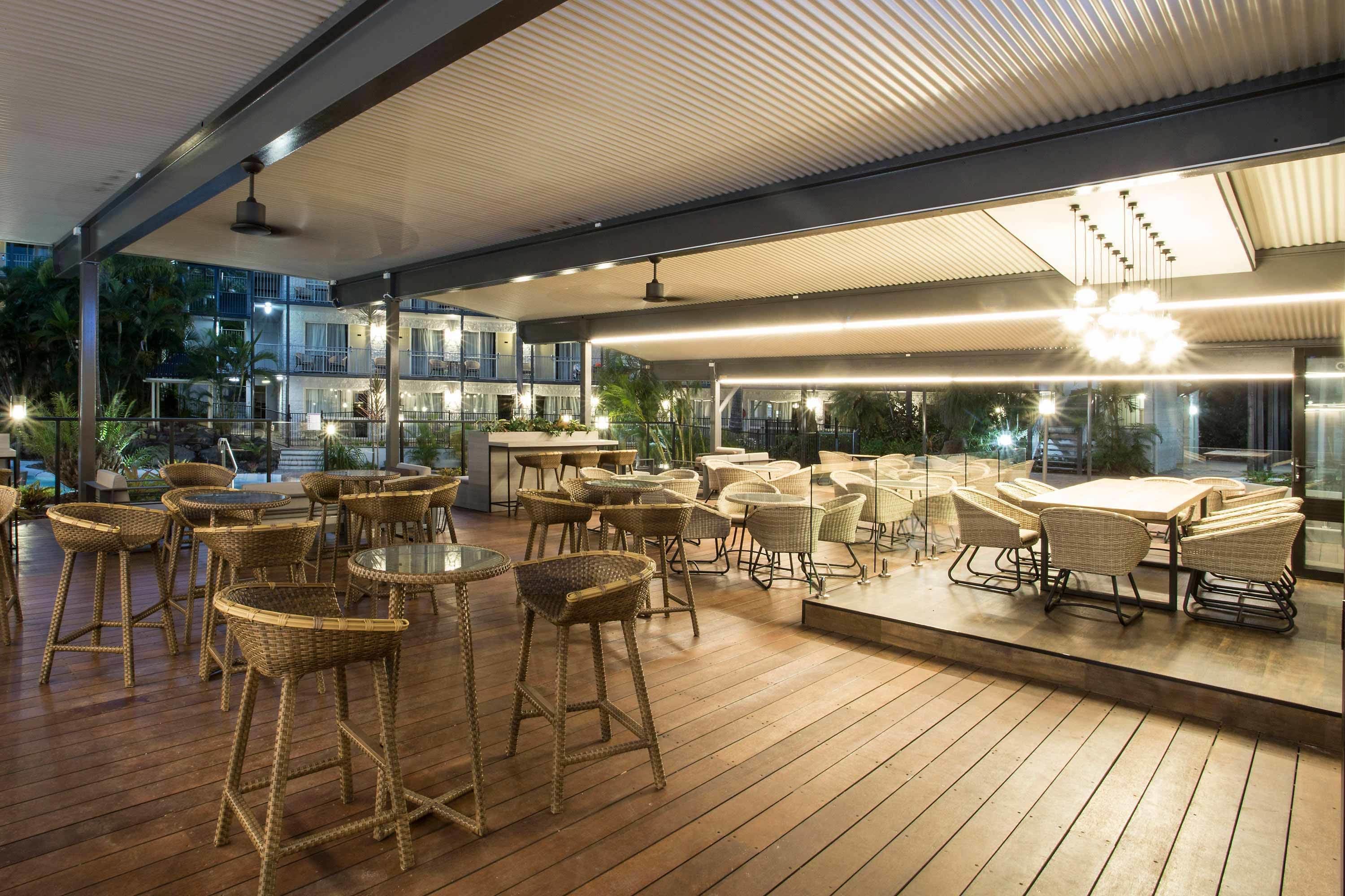 An outdoor patio area with wicker furniture, glass tables, and a view of the building in the background.