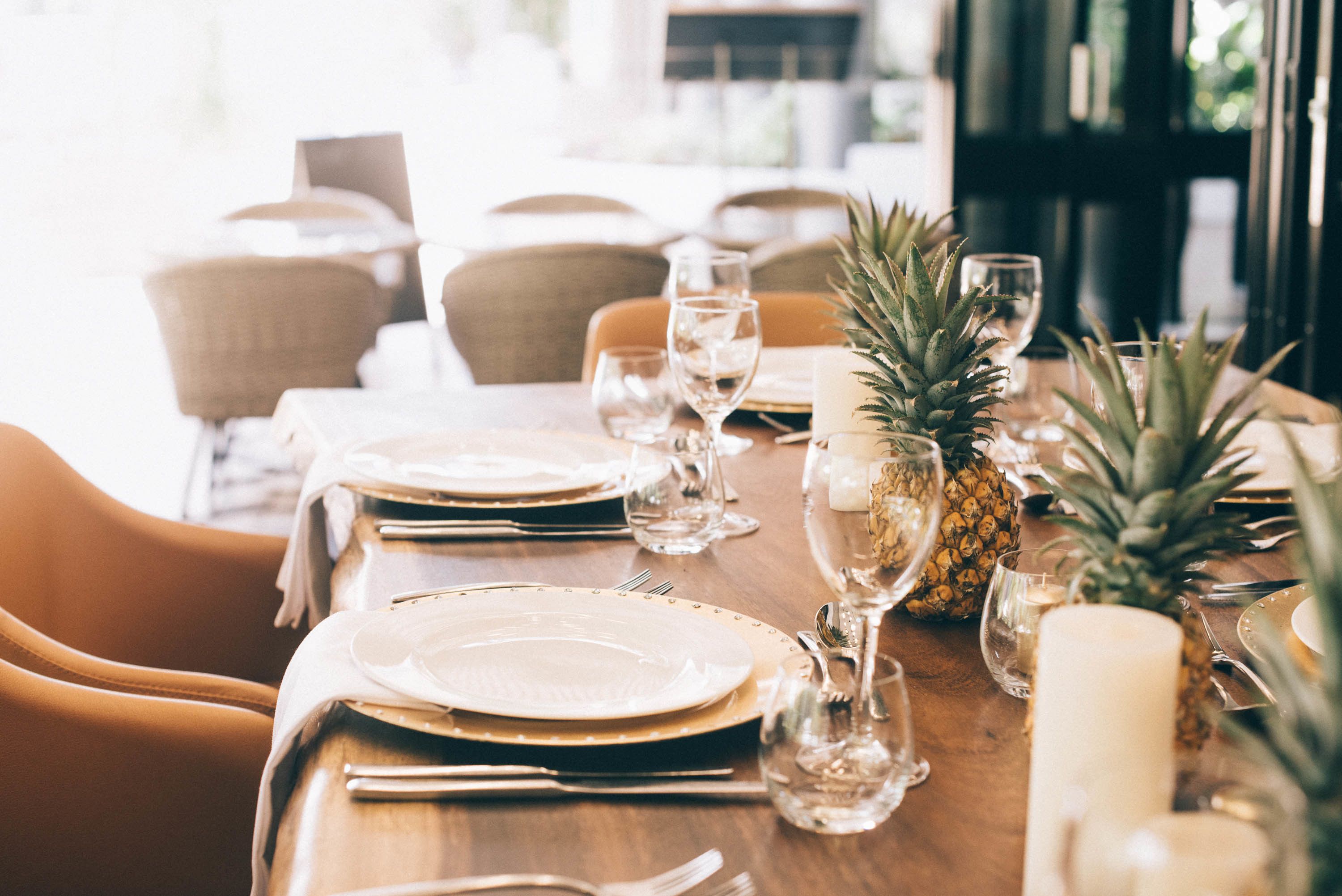 Una mesa de comedor dispuesta con platos, cubiertos, vasos y velas, rodeada de sillas.
