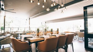 Restaurante con terraza, mesas dispuestas con velas y bebidas, y lámparas colgantes.