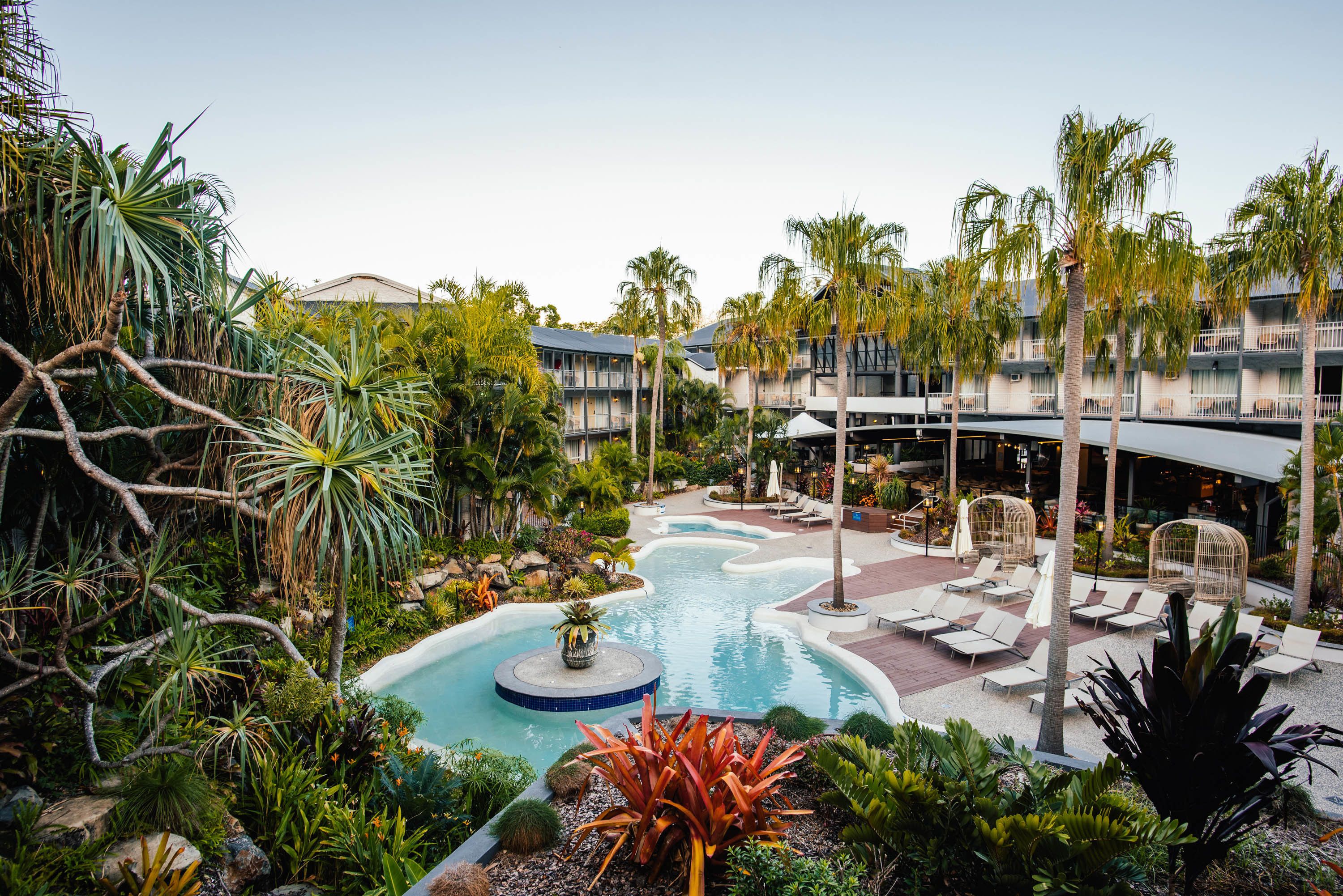 A resort with a swimming pool, lounge chairs, palm trees, and a landscaped garden.