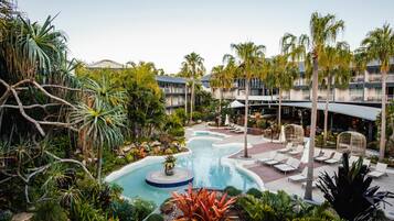 A resort with a swimming pool, lounge chairs, palm trees, and a landscaped garden.