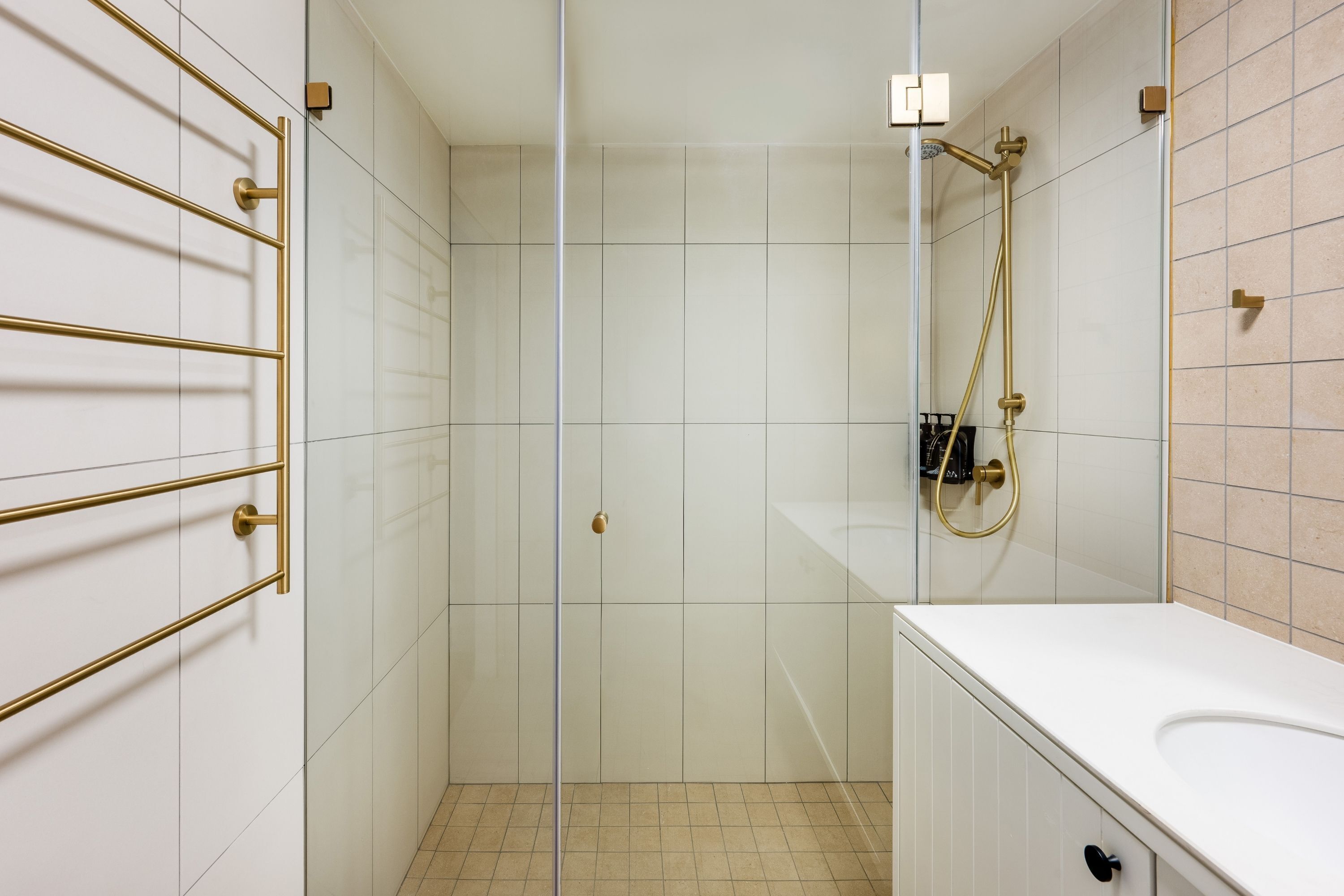 Un baño moderno con cabina de ducha de vidrio, azulejos blancos y detalles dorados.