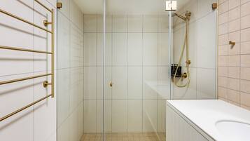 Een moderne badkamer met een glazen douchecabine, witte tegels en gouden details.
