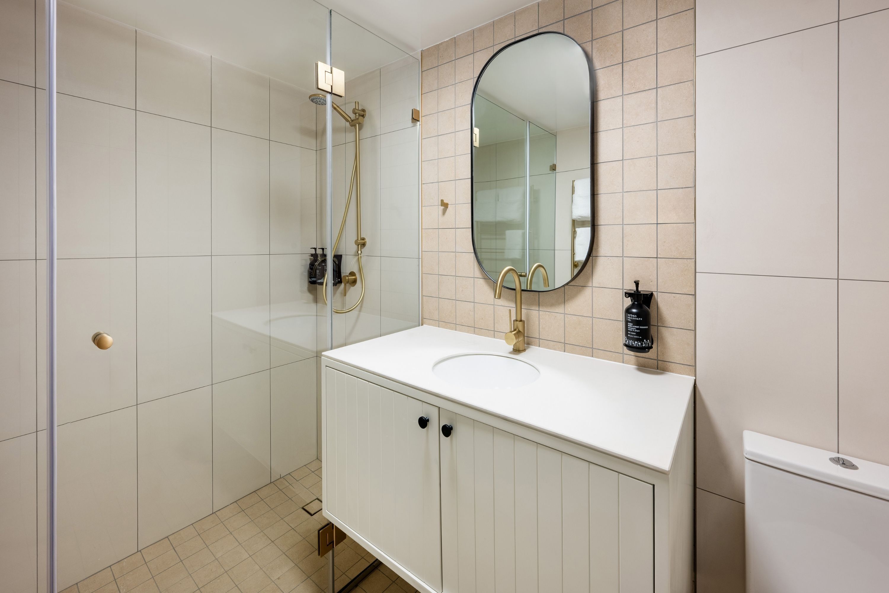 Un baño moderno con un tocador blanco, un espejo grande y una ducha.