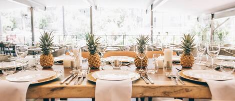 A dining table set with plates, cutlery, glasses, and candles, with pineapples on the table.