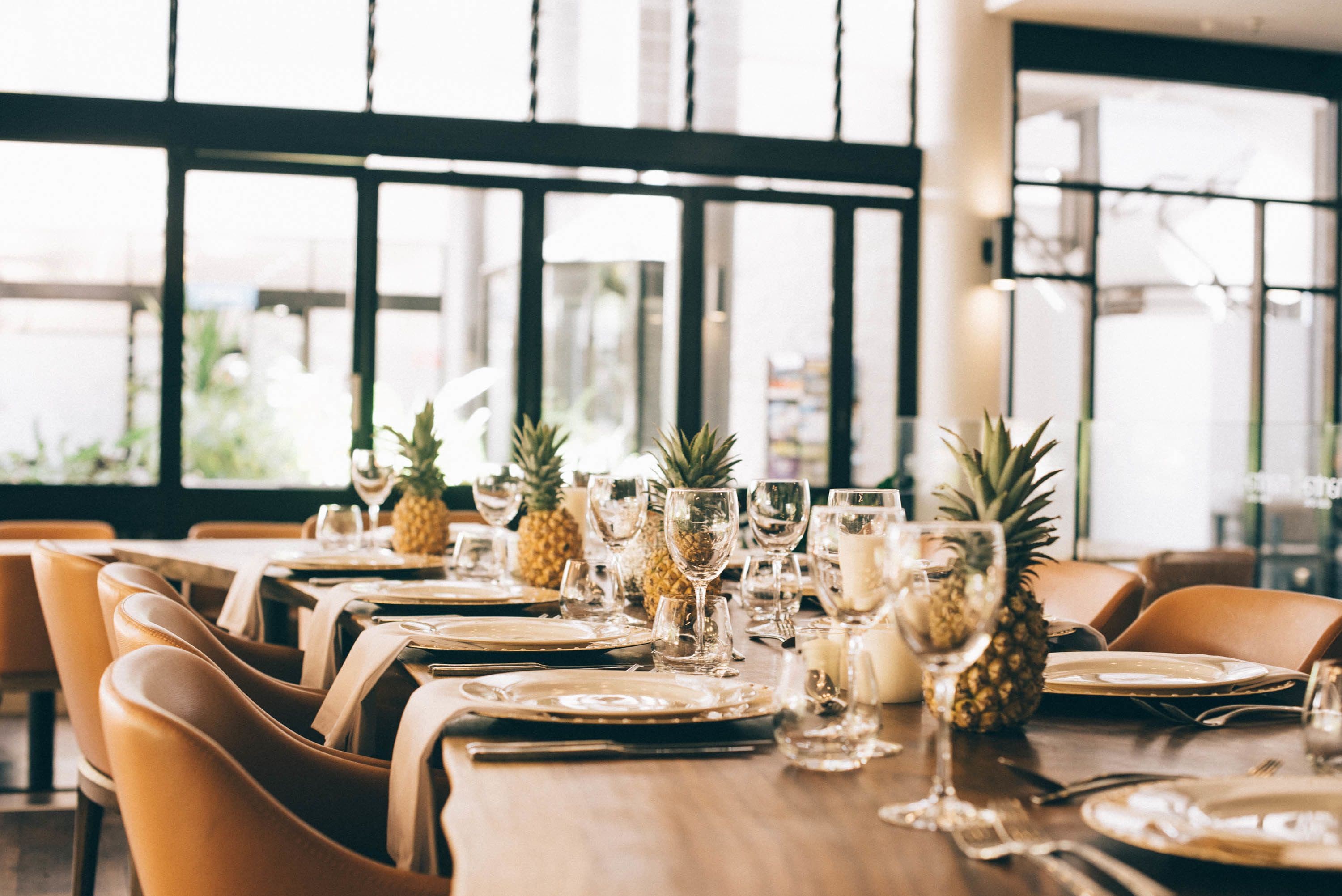 A dining table set with plates, cutlery, and glasses, with pineapples and candles on the table.