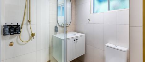 Un baño moderno con ducha de vidrio, un lavamanos blanco con espejo y un inodoro.