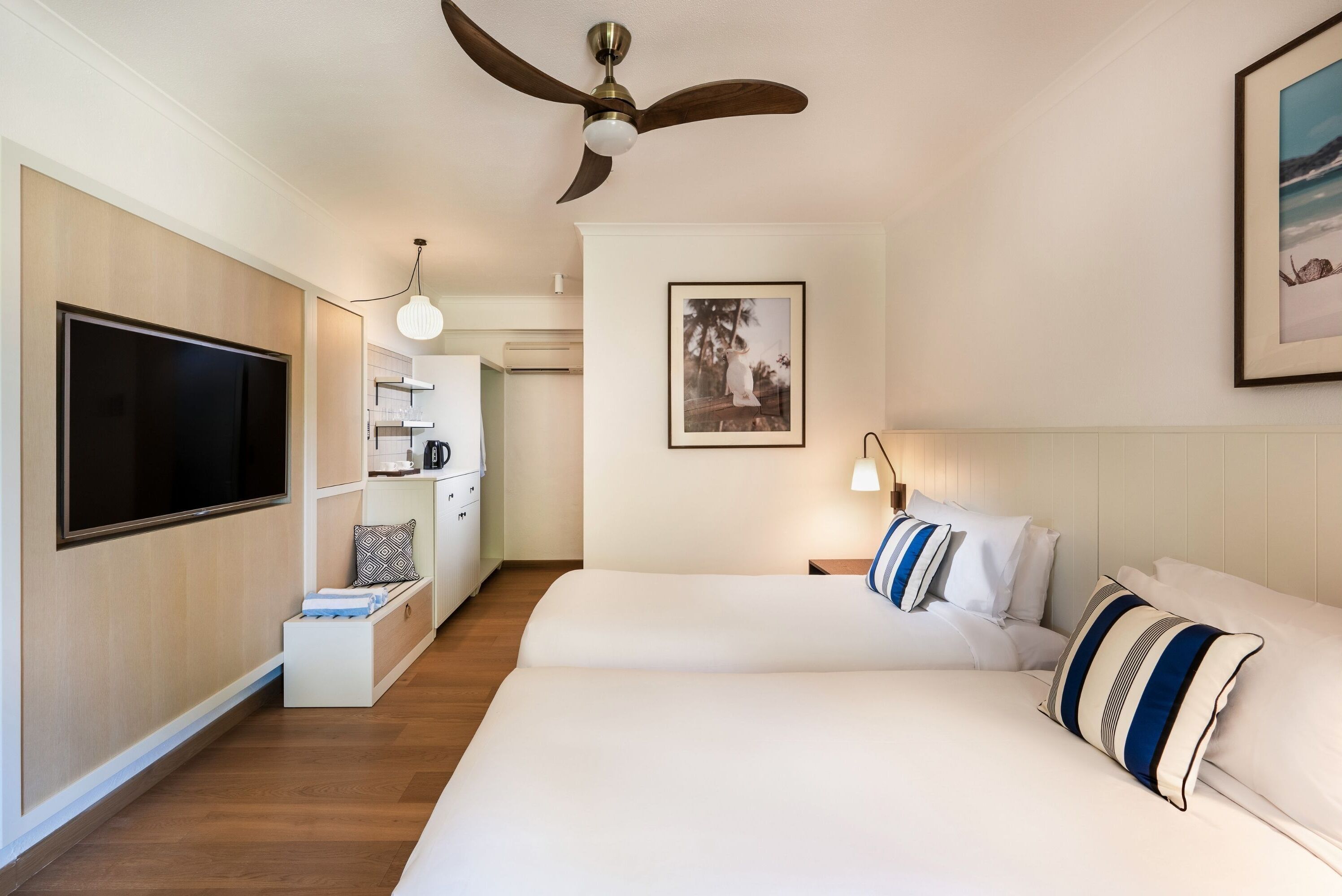 Habitación de hotel con una cama grande, un televisor, un ventilador de techo, un cuadro enmarcado en la pared y una mesita de noche con lámpara.