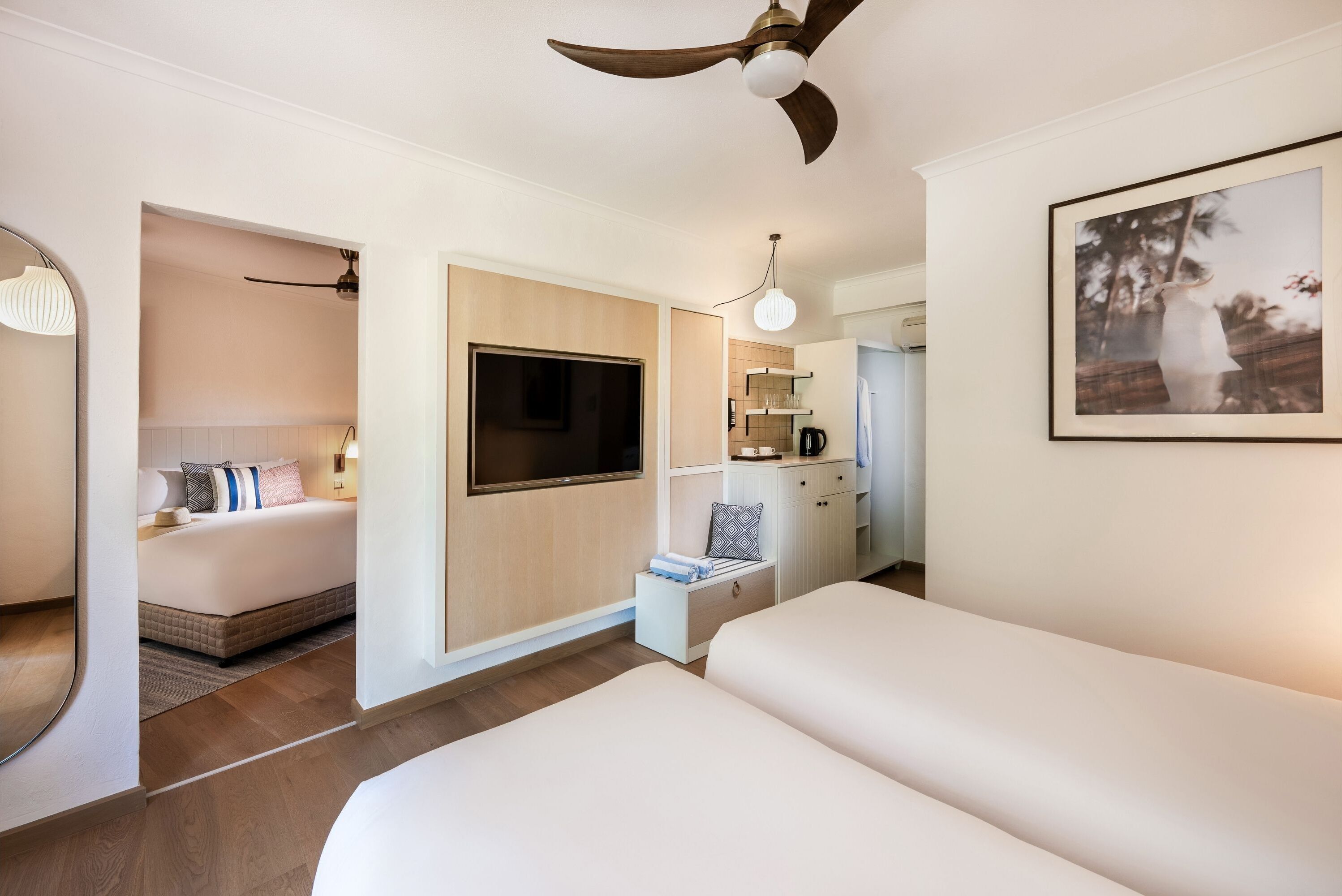 A hotel room with a large bed, a TV mounted on the wall, a ceiling fan, a small seating area with a table and chairs, and a framed picture on the wall.