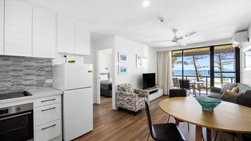 A modern kitchen with a built-in oven, a dining area with a round table, and a view of the ocean through large windows.