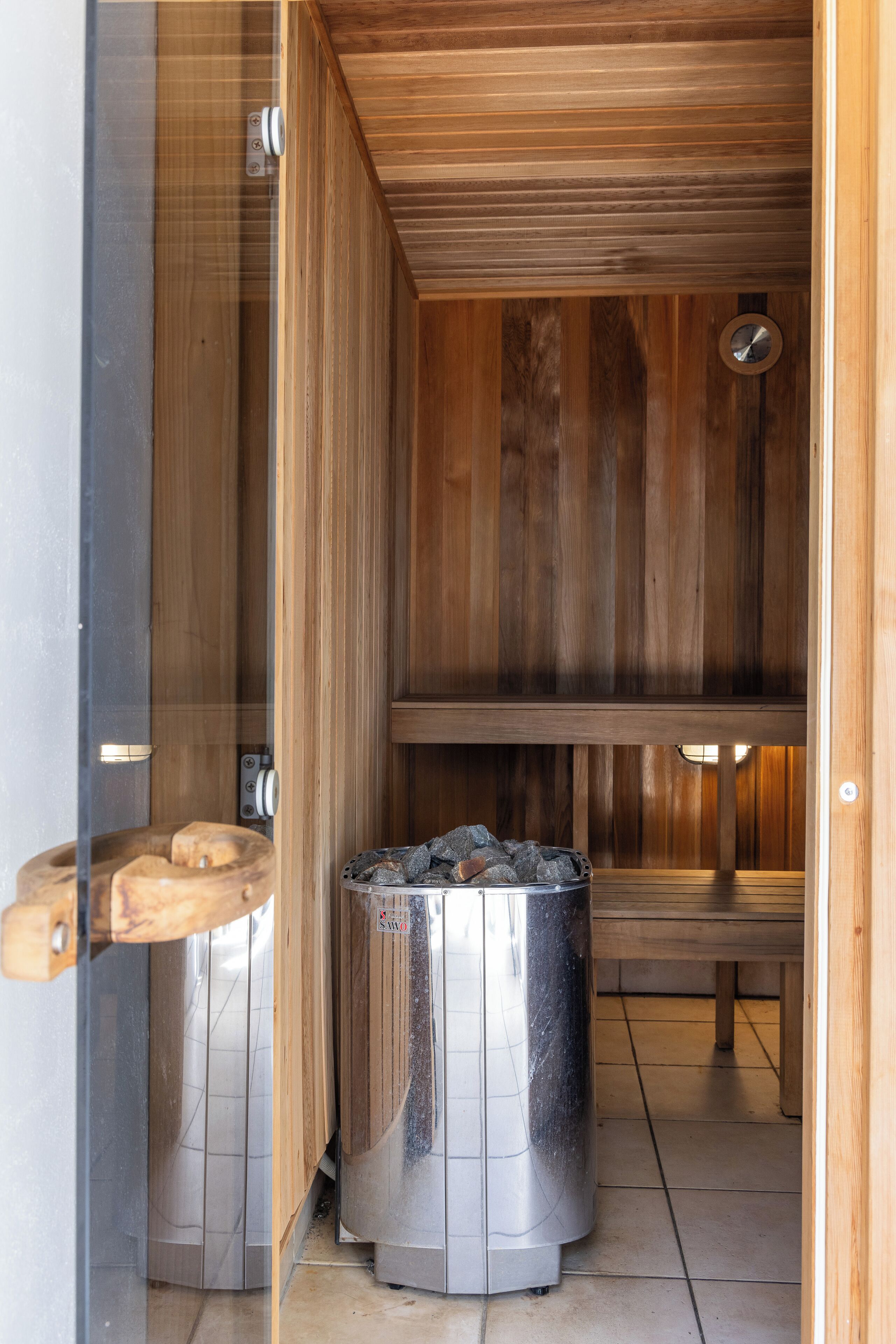 A sauna with wooden walls, a bench, and a metal container with rocks.