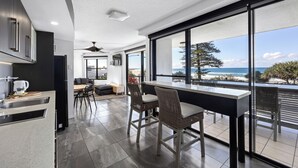 A modern kitchen with dark cabinetry and a large window overlooking the ocean. - Beach Retreat Coolum (Coolum Beach)