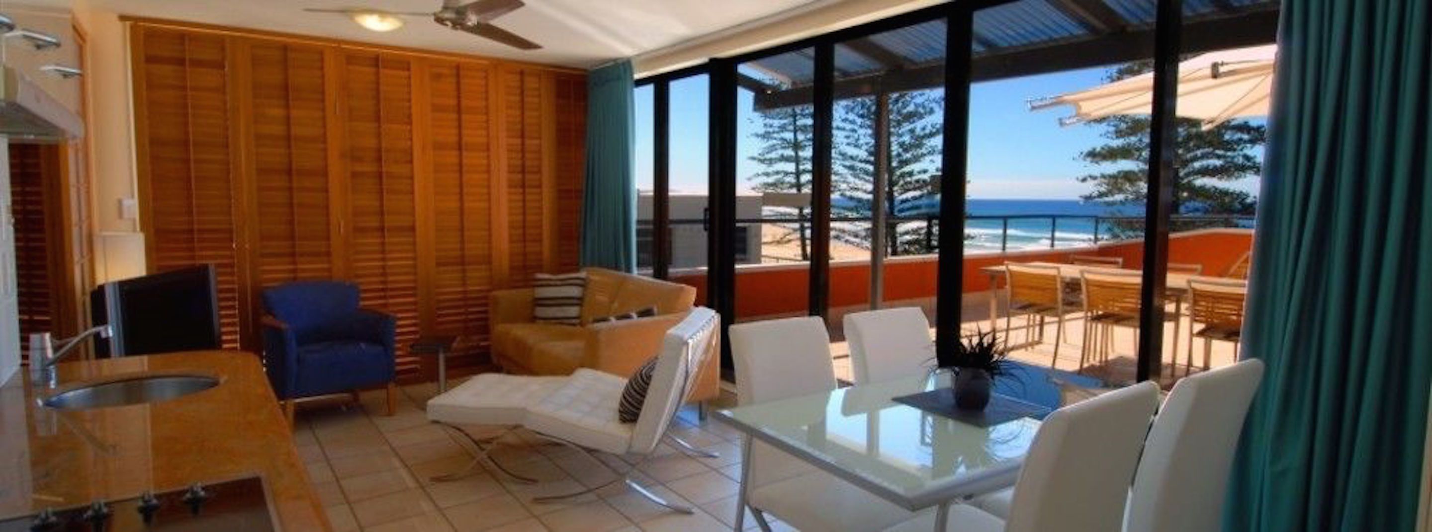 A room with a view of the ocean, a ceiling fan, a wooden wall, and a table with chairs.