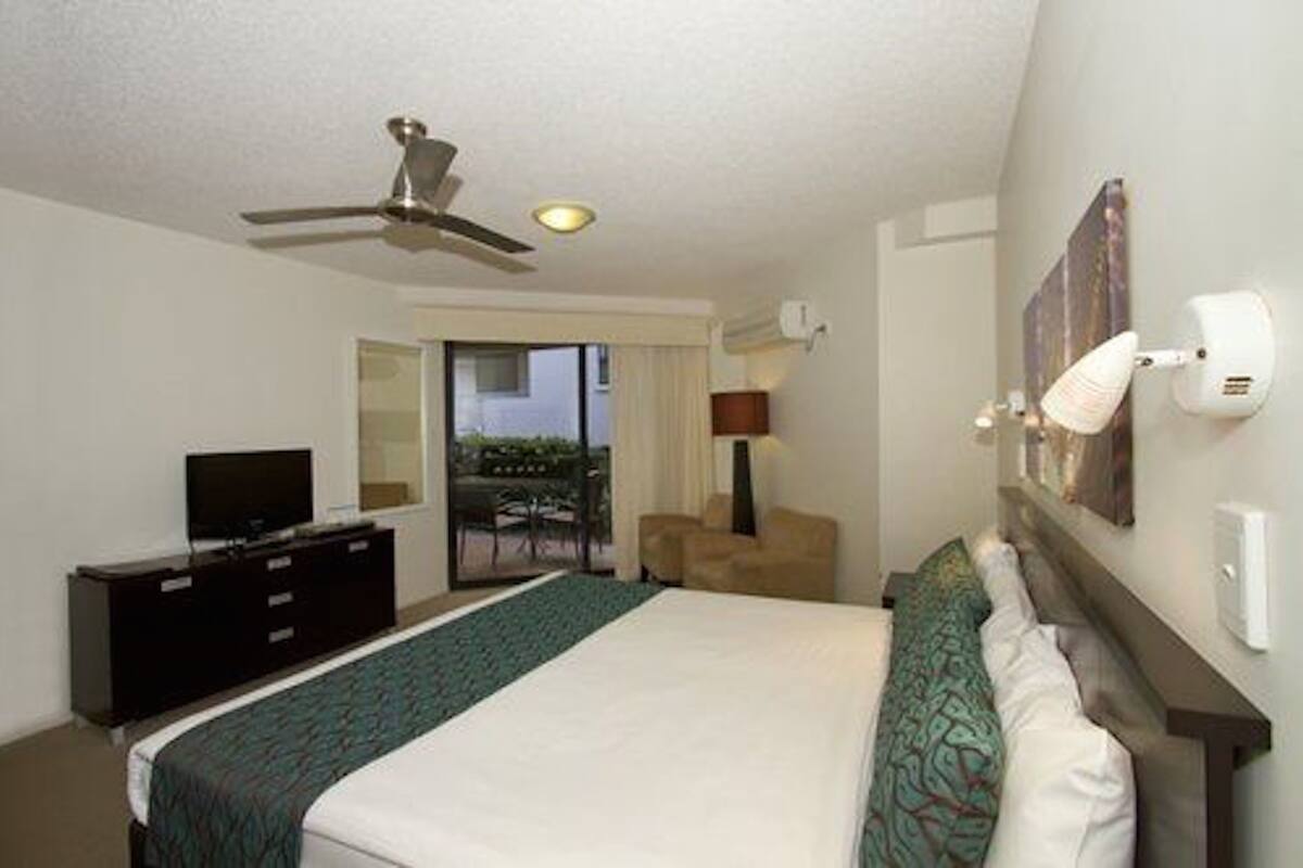 A hotel room with a bed, a TV, a ceiling fan, a desk, and a chair.