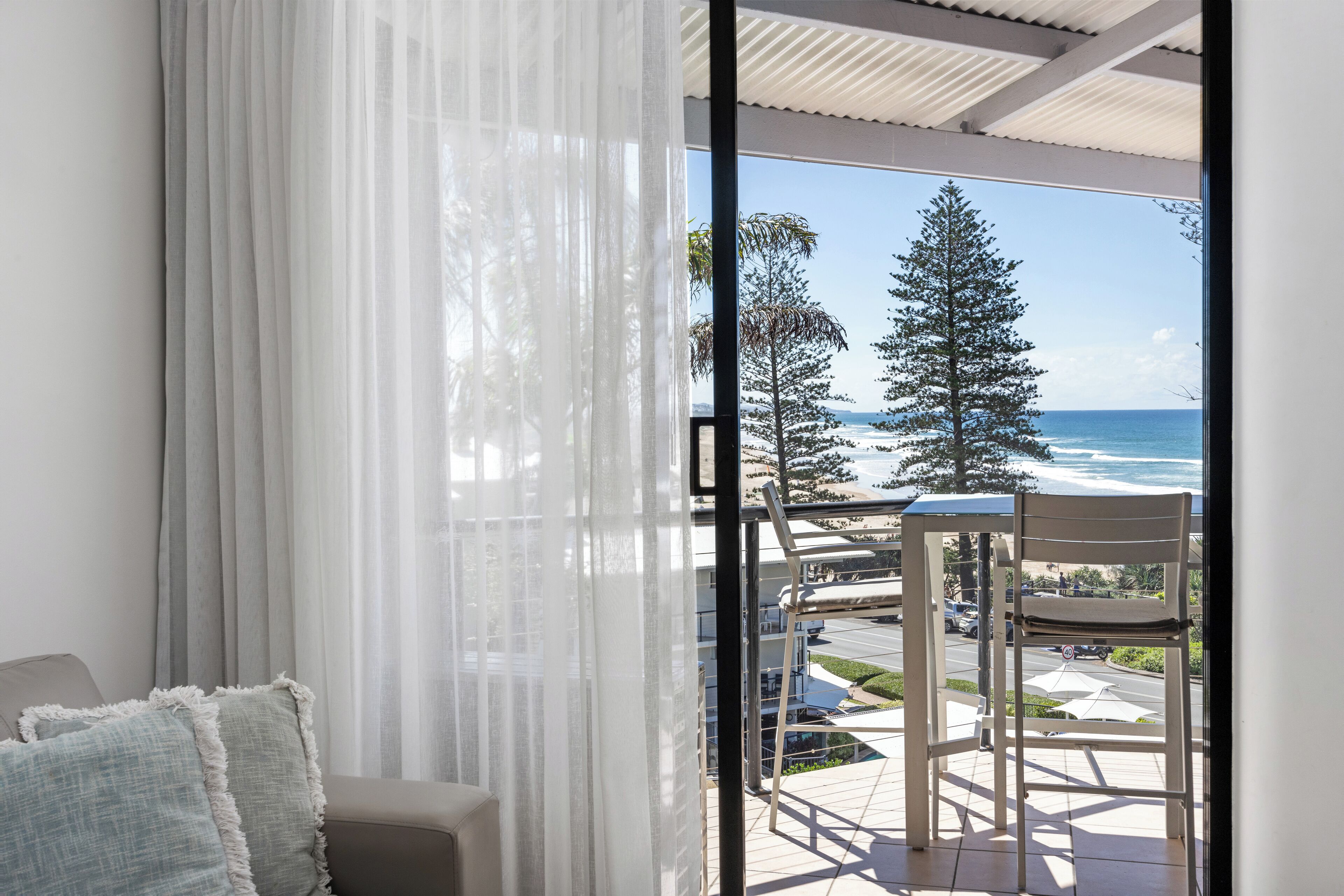A balcony with a view of the ocean and trees, a chair, and a table.