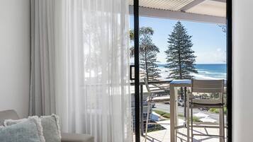 A balcony with a view of the ocean and trees, a chair, and a table.